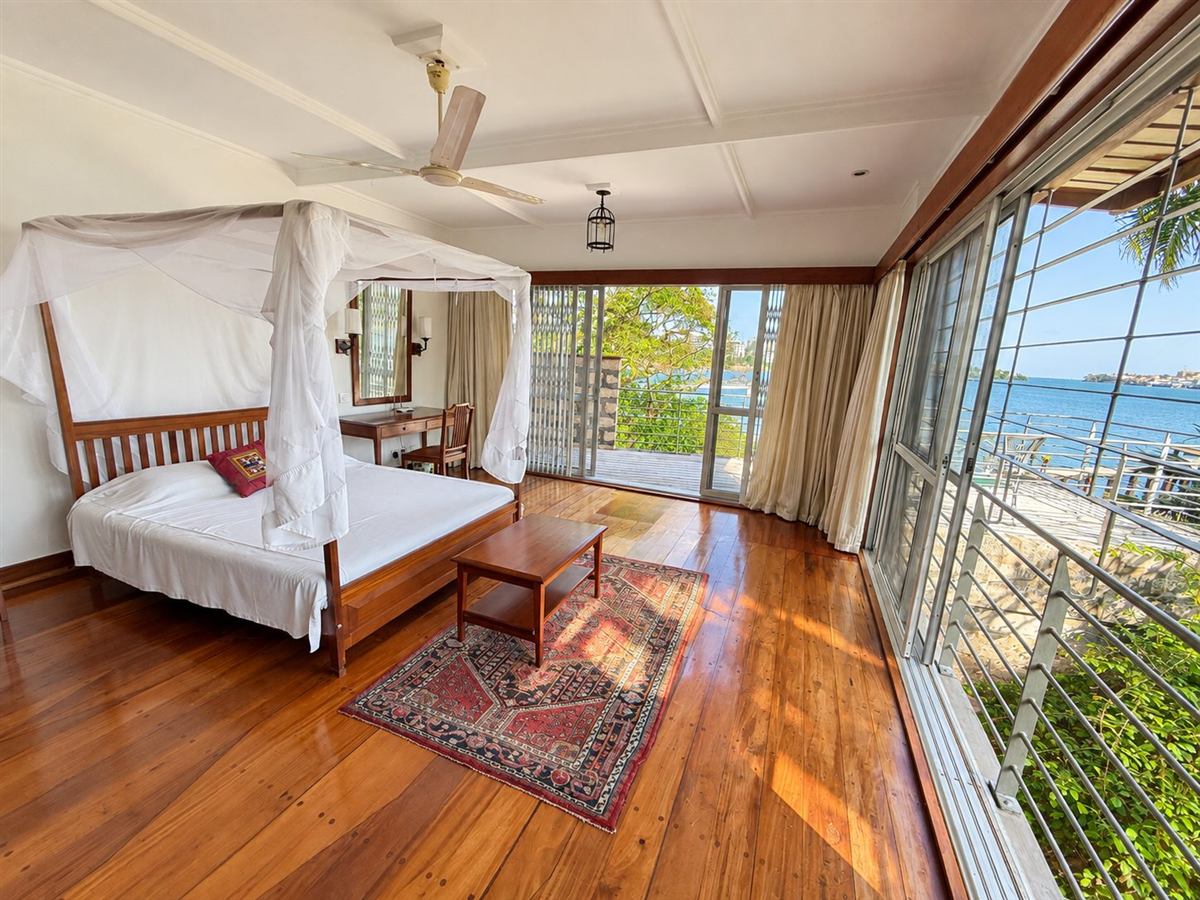 Bedroom with a four-poster bed, timber floor and windows onto the creek