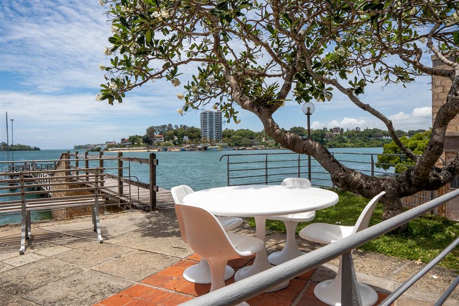 A white table and chairs on the terrace at water level, under a frangipani