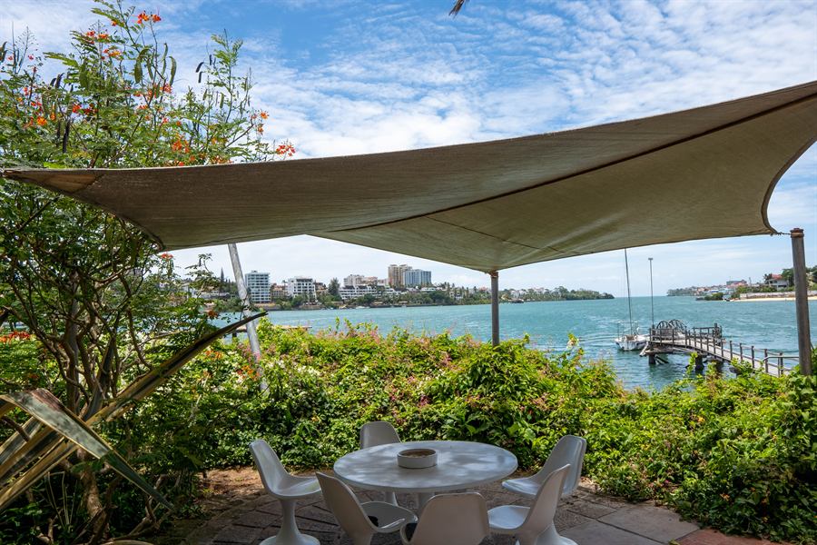 A table under a shade sail, looking out over the jetty and the creek